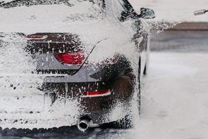 Horizontal shot of car covered with soap foam. Cleaning service. Water pressure on automobile. Manual car washing. High pressure cleaning photo