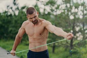 un joven y apuesto hombre europeo fuerte posa en el estadio del parque, estira la cuerda, tiene el torso desnudo y los brazos musculosos, va a hacer ejercicios físicos, posa al aire libre. concepto de entrenamiento callejero foto