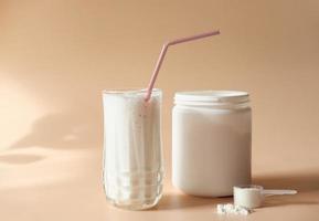 whey drink in a high glass. whey protein vanilla cocktail. a jar with protein powder and a scoop of powder on a table. morning drink for health and beauty photo