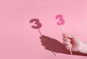 girl's hand holding a number 3 shaped lolipop. photo