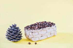 unpeeled cedar nuts in wicker basket next to cone on yellow background. rich in unsaturated fats food for brain boost and heart health. raw food for paleo diet. vegetarian meal plan