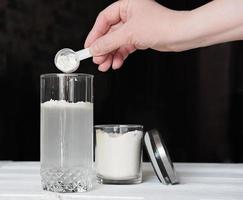 female hand woman making whey protein drink in a glass and jar with protein powder. supplement for healty joints and beauty. crop view, vegan dietary cocktail photo