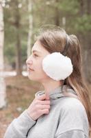 Outdoor portrait of teenager girl wearing white earmuffs. close up of a girl walking in the forest. teen looking aside. hiking and tracking alone. generation z concept. side view photo