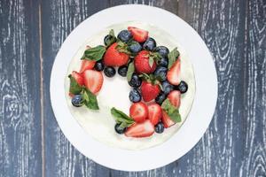 vista superior de la torta horneada para la selebración de cumpleaños o aniversario. decoración fresca de fresas y arándanos con hojas de menta foto