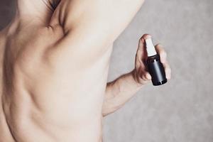 hombre musculoso tonificado usando desodorante corporal para frescura y confianza durante todo el día. Desodorante en spray antitranspirante natural para hombre. joven en forma sin camisa, vista recortada foto