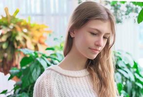 calm and pensive teenager girl looking aside and walking. home green plants on a background. beautiful caucasian teenager wearing white casual pullove photo