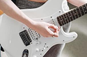 female artist playing electric guitar performing a song. crop view. woman with white guitar rehearsing at home. music as hobby and creative leisure. photo