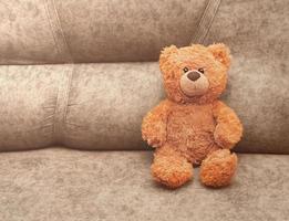 teddy bear toy sitting on a sofa and looking at a viewer. children safety and loneliness concept, kids best friend photo