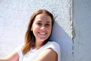 young adult woman smiling and looking at camera. freckled caucasian woman sitting next to an old house wall and enjoying summer photo