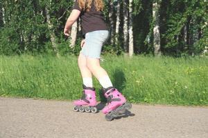 teenager girl practicing in rollerskating in a summer park. partial view. pink inline rollers. teen leisure and sports photo