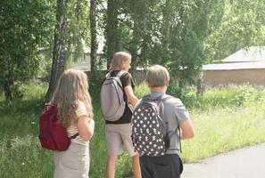 rear view of teenagers going to high school. generation z concept. a teen girl with long curly hair and two boys coming forward with backpacks photo