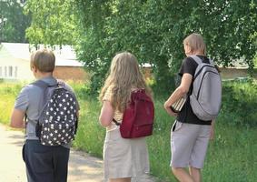 rear view of teenagers going to high school. generation z concept. a teen girl with long curly hair and two boys coming forward with backpacks photo