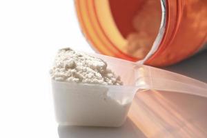 scoop of whey protein and jar with protein powder. vanilla flavored supplement for healty lifestyle, close up view photo