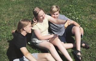 three teenagers making selfie sitting on a grass. teen girl holding a smartphone camera. friendship and togetherness concept. photo