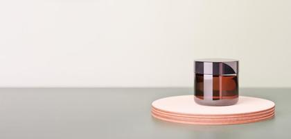 face cream in amber glass jar on a wooden podium or pedestal on green background. mock up for natural eco product presentation. photo