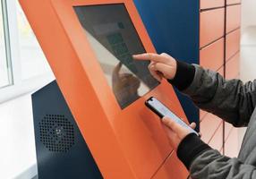 client using automated self service post terminal machine or locker to receive a parcel or to deposit the box. contactless delivery to pick up point photo