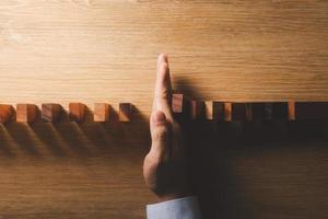 Risk management and business strategy concept, businessman hands stop the dominoes from falling continuously, preventing future risks from crisis. photo