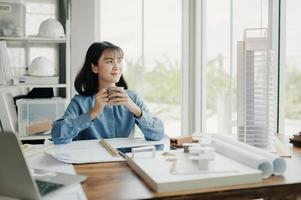 Selective focus, Young Asian architect or engineer drinking tea, coffee during a break in planning the blueprints of building structures. architect or engineer design projects in the office. photo