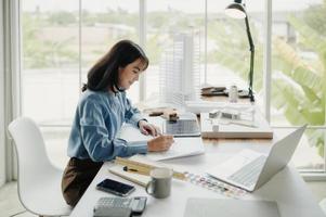 Selective focus, Asian female architect or engineer Drawing the design of the building structure in the blueprint. Asian female architect or engineer Sit and analyze, design projects in the office. photo