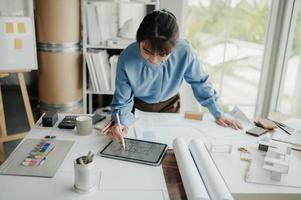 Selective focus, Asian female architect or engineer Drawing the design of the building's interior using a tablet. Asian female architect or engineer Sit and analyze, design projects in the office. photo