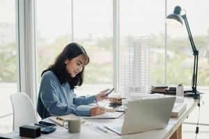 enfoque selectivo, arquitecta o ingeniera asiática que actualmente considera materiales para diseñar condominios modernos. arquitecta o ingeniera asiática sentada y analizando, diseñando proyectos en la oficina foto