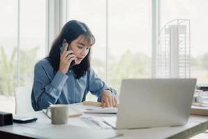 Selective focus, Asian female architect or engineer Talking on the phone with the team planning design of the building structure in the blueprint. architect or engineer design projects in the office. photo