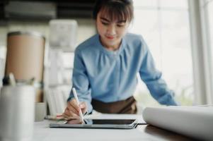 Selective focus, Asian female architect or engineer Drawing the design of the building's interior using a tablet. Asian female architect or engineer Sit and analyze, design projects in the office. photo