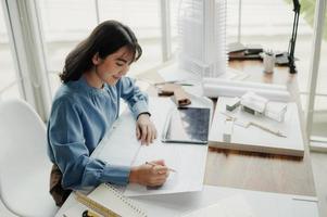 enfoque selectivo, arquitecta o ingeniera asiática dibujando el diseño de la estructura del edificio en el plano. una arquitecta o ingeniera asiática se sienta y analiza, diseña proyectos en la oficina. foto