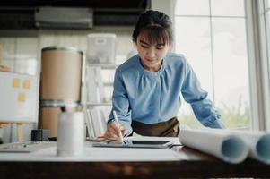 Selective focus, Asian female architect or engineer Drawing the design of the building's interior using a tablet. Asian female architect or engineer Sit and analyze, design projects in the office. photo