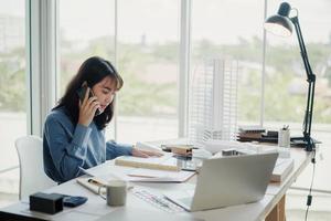 Selective focus, Asian female architect or engineer Talking on the phone with the team planning design of the building structure in the blueprint. architect or engineer design projects in the office. photo