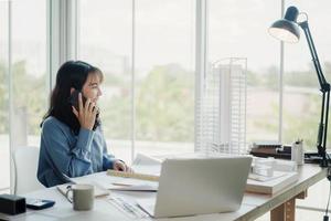 Selective focus, Asian female architect or engineer Talking on the phone with the team planning design of the building structure in the blueprint. architect or engineer design projects in the office. photo