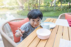 Happy Asian boy looking at camera is smiling enjoying pointing fingers up sitting on the chair. Concept of happy family or successful adoption or parenting photo