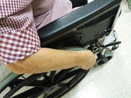 An senior or elderly woman is sit on wheelchair and her hand holding on the wheel of the wheelchair