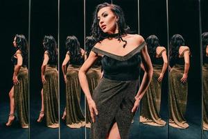 Portrait of beautiful brunette woman in golden dress standing near the mirrors. Fashion, style concept photo