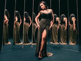 Portrait of beautiful brunette woman in golden dress standing near the mirrors. Fashion, style concept photo