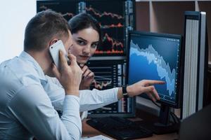 Command requires a report on the phone. Team of stockbrokers are having a conversation in a office with multiple display screens photo