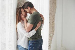 In strong man's hands. Lovely couple kissing and enjoying each other near the window of their new home photo