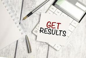 get results - text on white sticker and calculator with pen on wooden background