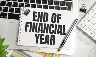 End of Financial Year . text on white paper and laptop on wooden background photo