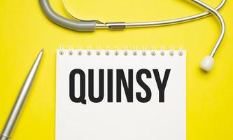 The word qUINSY written on a white notepad on a yellow background photo