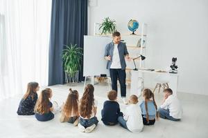 de pie y explicando la lección usando una pizarra. grupo de niños estudiantes en clase en la escuela con el maestro foto