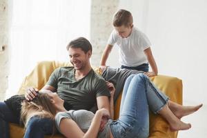 gente exitosa. familia feliz diviértete en el sofá amarillo en la sala de estar de su nueva casa foto