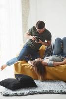 se ve bien. fotógrafo tomando una foto de una joven que yacía en el sofá blanco