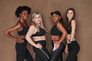 Hands on the waists. Group of multi ethnic women standing in the studio against brown background photo