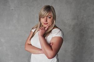 mirada pensativa. joven mujer blanca en el estudio de pie contra el fondo gris foto