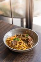 Tagliatelle with pork stew and vegetables in a bowl served on wooden table photo