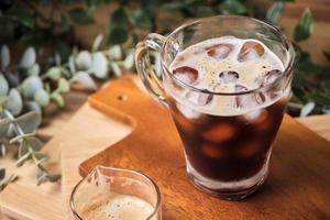 cold iced black brew coffee in a glass with pieces of ice on a wooden table, natural light, fresh summer drink in the morning photo