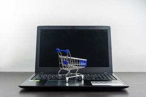 computadora portátil pantalla en blanco con carrito de compras en la mesa de madera foto