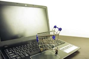 computadora portátil pantalla en blanco con carrito de compras en la mesa de madera foto