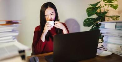 Workaholic people concept. Asian woman drinking coffee during overtime photo